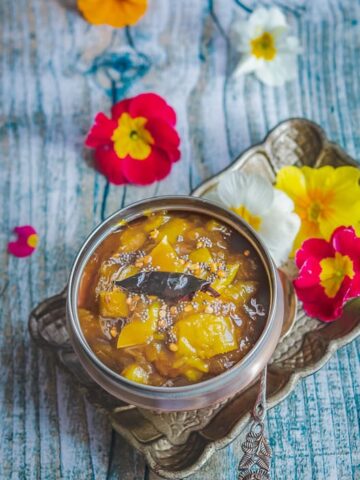 raw mango pachidi served in a copper bowl and a tray full of flowers.