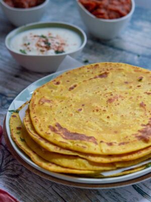 Besan masala roti or gram flour roti is stacked on a plate with yogurt and tomato curry on the side.